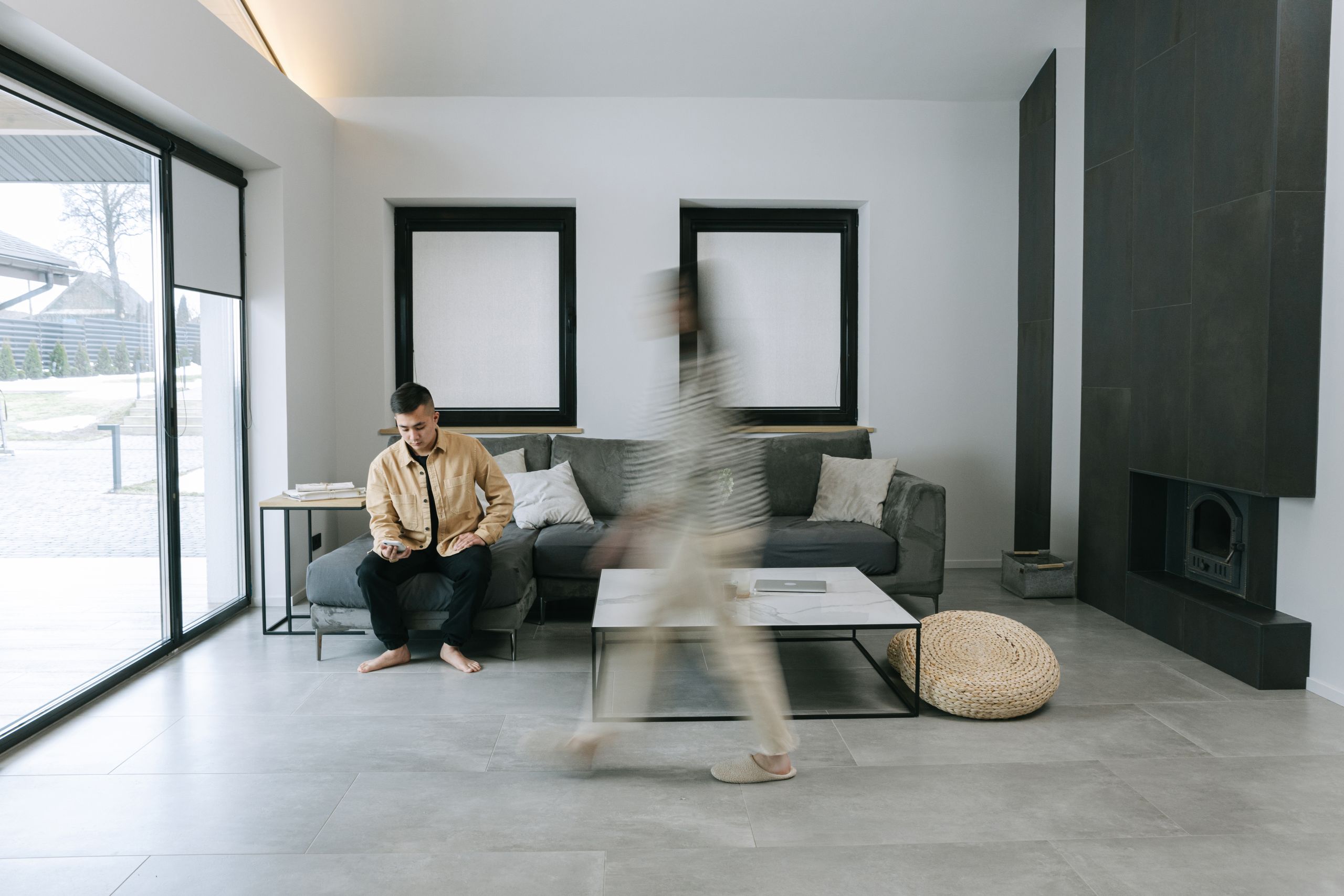 Dos personas dentro de una vivienda contemporánea: una cruza la sala en movimiento y otra está sentada junto al ventanal